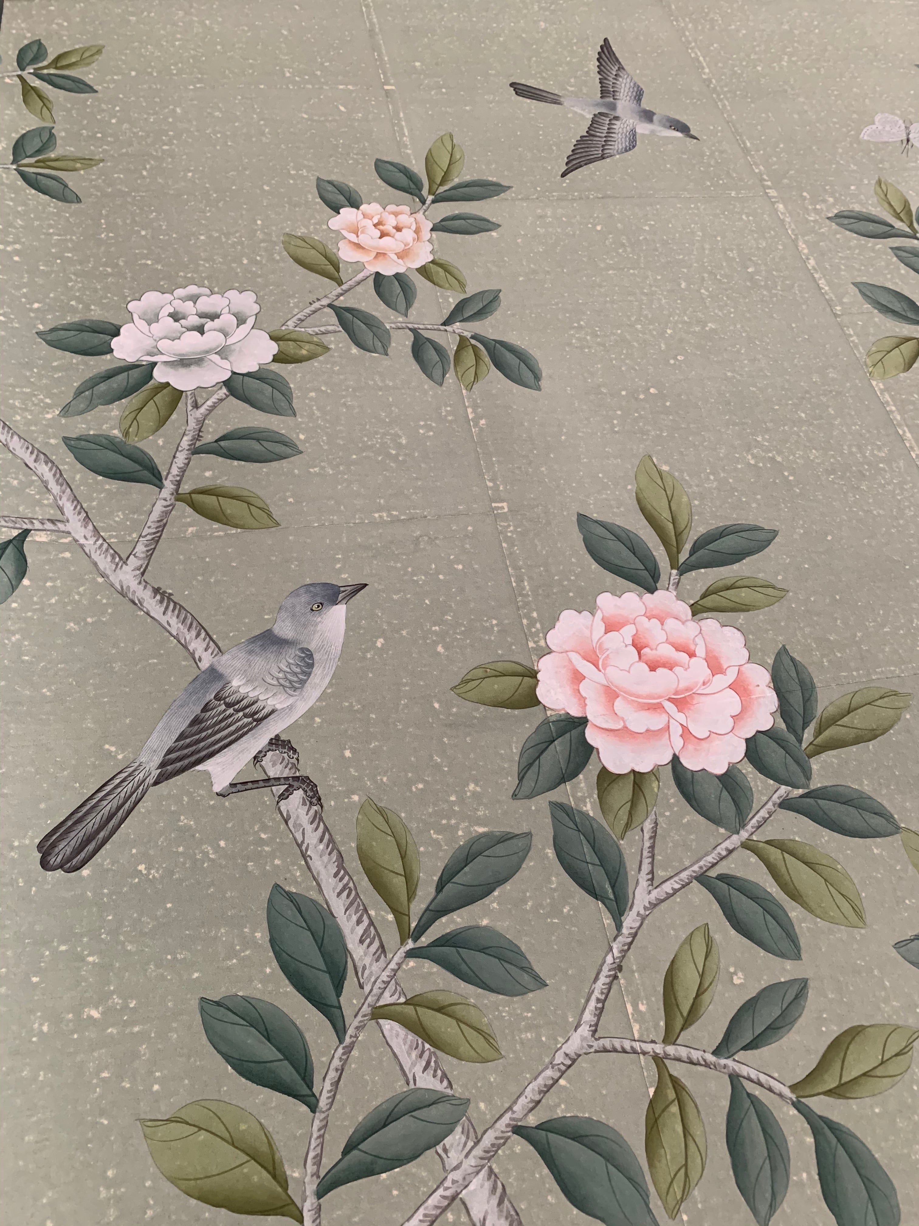 Close-up of hand-painted chinoiserie wallpaper on antique green tea paper, featuring delicate camellia blossoms and perched songbirds with soft brushwork and subtle gilded texture.