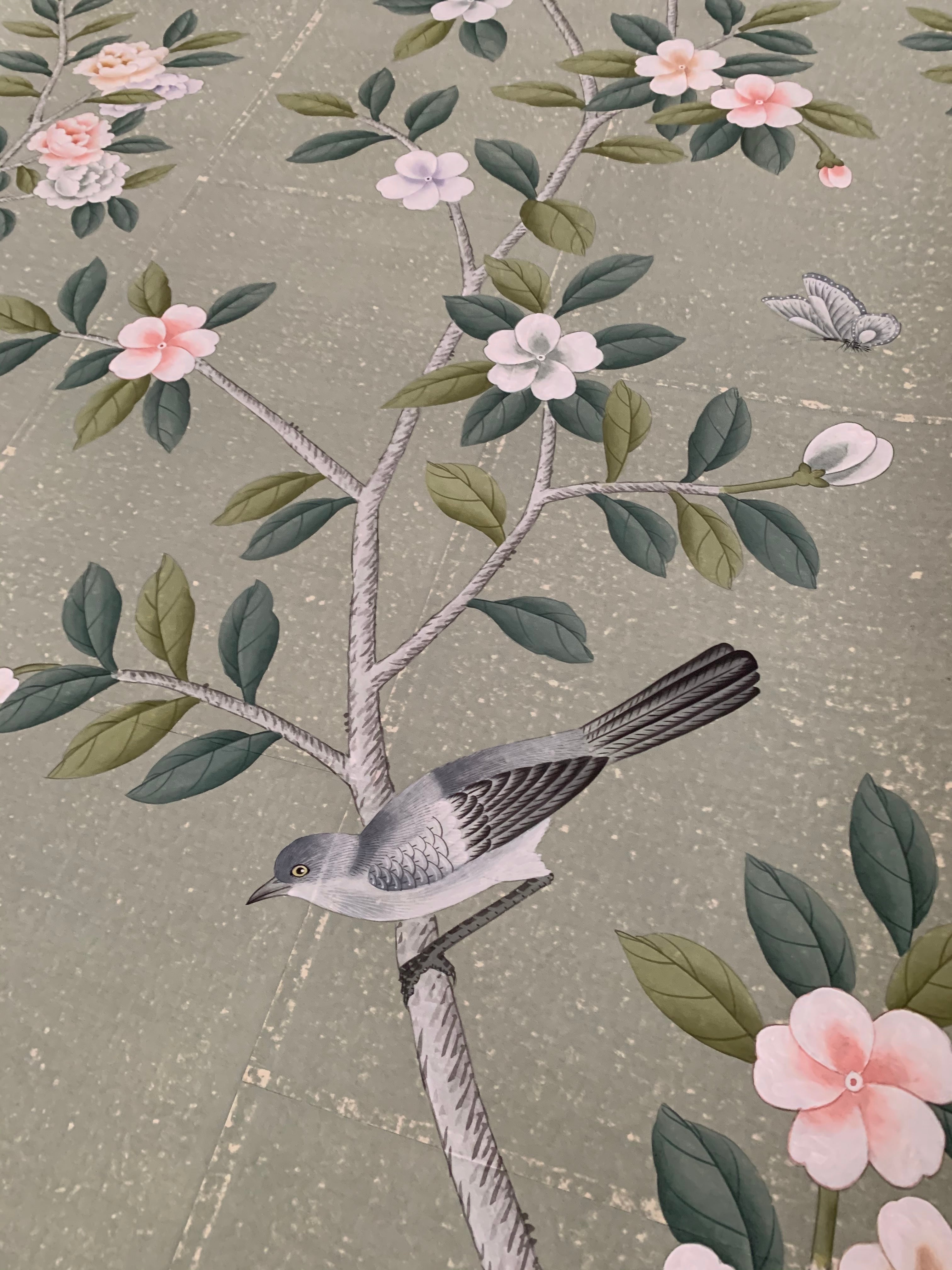Close-up of hand-painted chinoiserie wallpaper on antique green tea paper, featuring delicate camellia blossoms and perched songbirds with soft brushwork and subtle gilded texture.