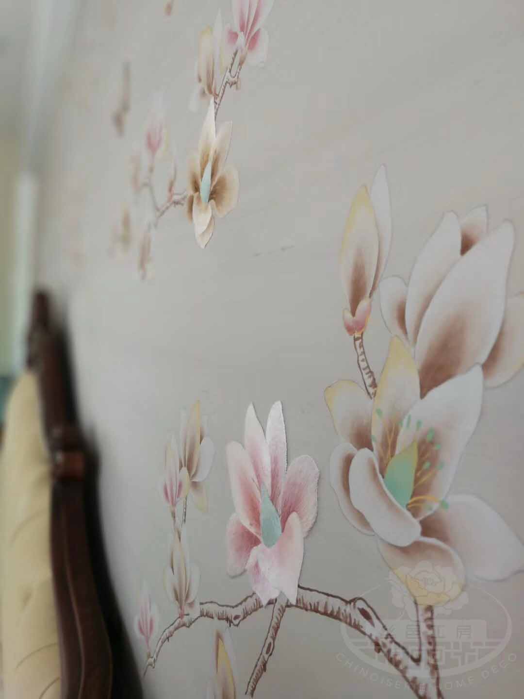Hand-painted magnolia and butterfly mural with partial embroidery, installed as bedroom headboard backdrop on neutral-toned wallpaper