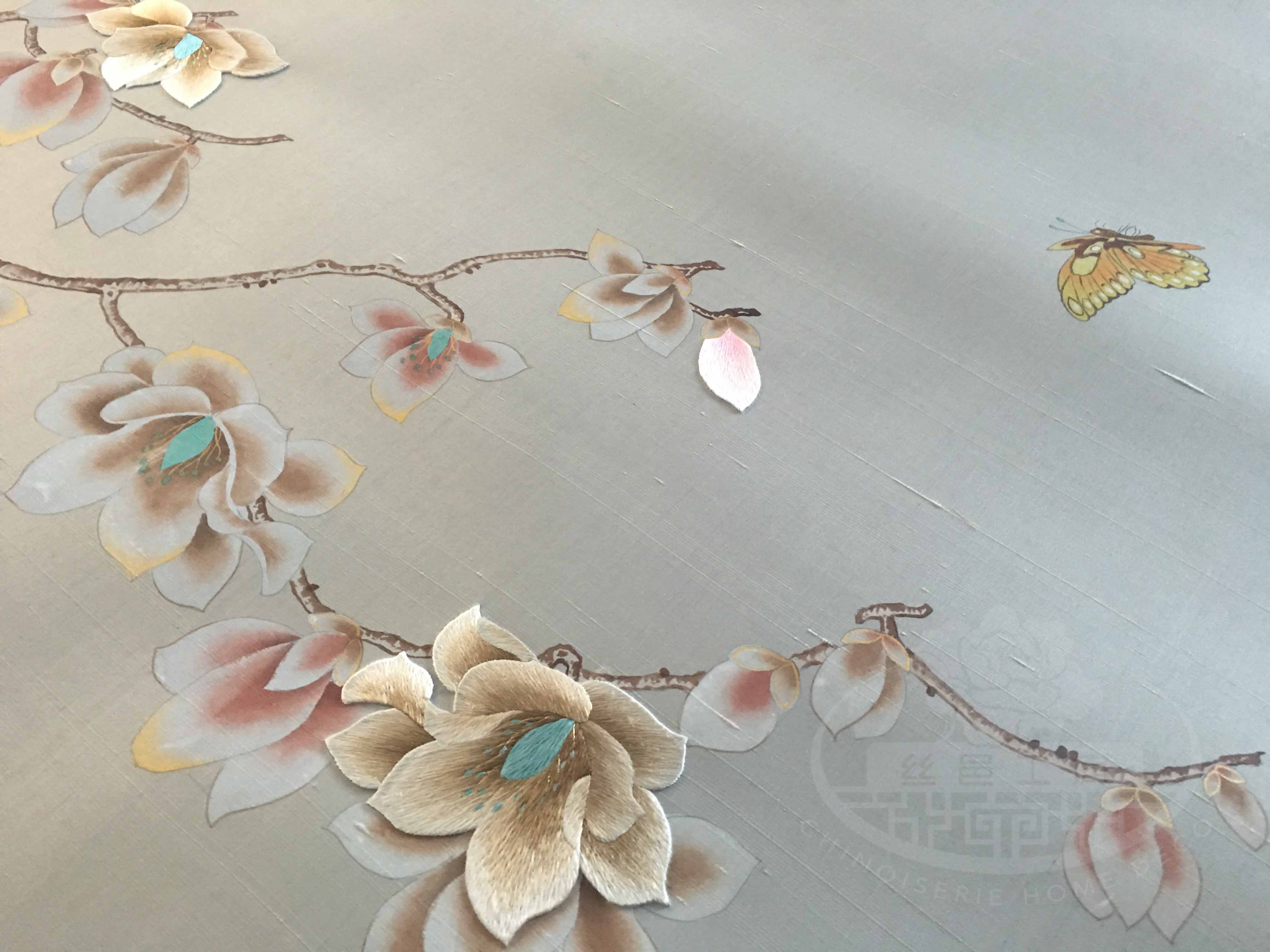 Hand-painted magnolia and butterfly mural with partial embroidery, installed as bedroom headboard backdrop on neutral-toned wallpaper