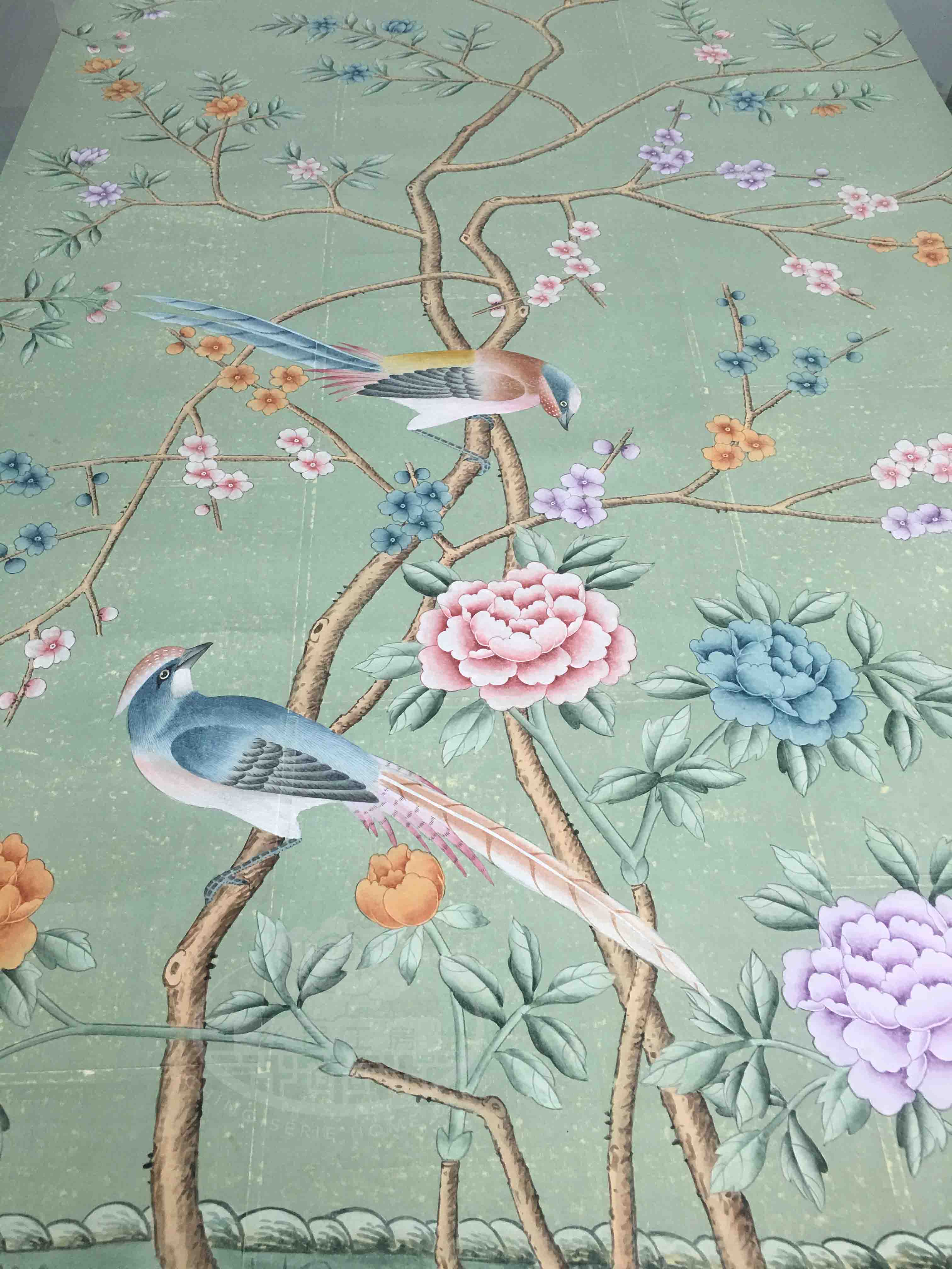 Close-up of handpainted chinoiserie wallpaper on antiqued tea paper, showing detailed brushwork of birds perched among flowering branches with soft green background.