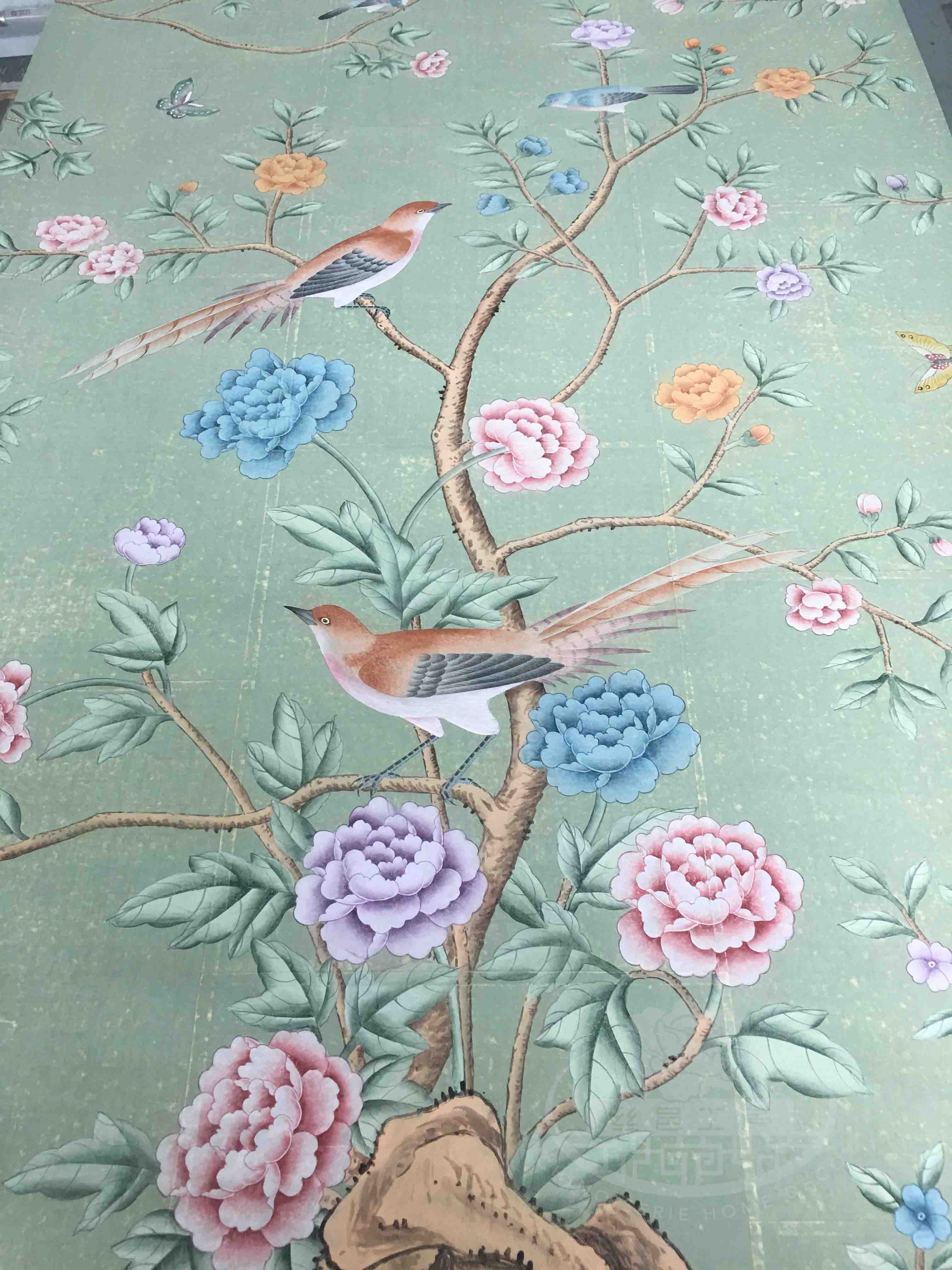 Close-up of handpainted chinoiserie wallpaper on antiqued tea paper, showing detailed brushwork of birds perched among flowering branches with soft green background.