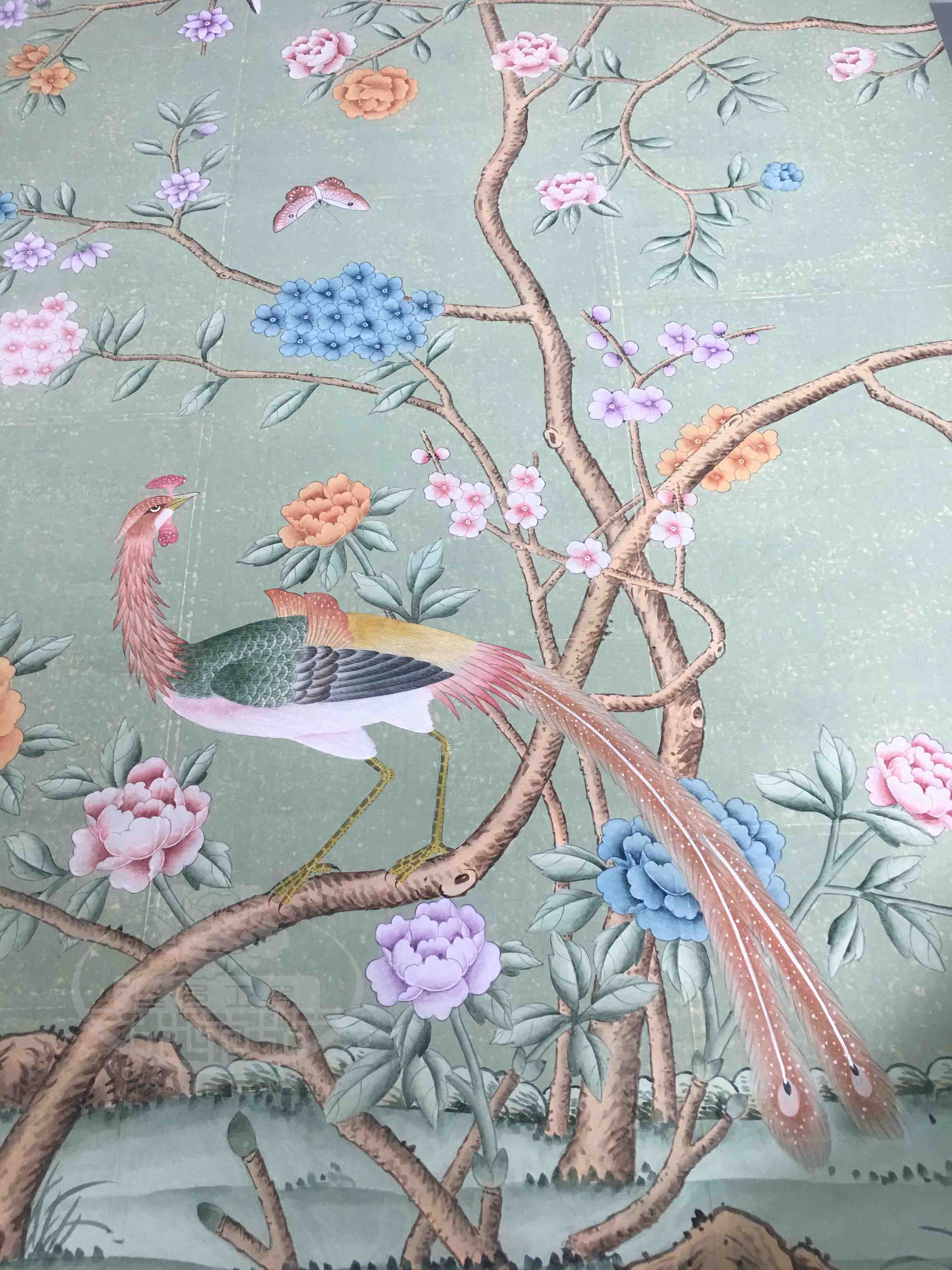 Close-up of handpainted chinoiserie wallpaper on antiqued tea paper, showing detailed brushwork of birds perched among flowering branches with soft green background.